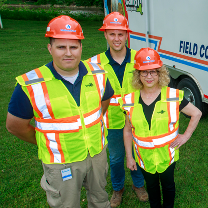 group of three people in hard hats and vests in front of field command center trailer