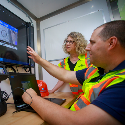 man pointing to computer showing woman an image on a tv