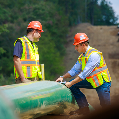 two men talking at a worksite wearing hard hats and vests